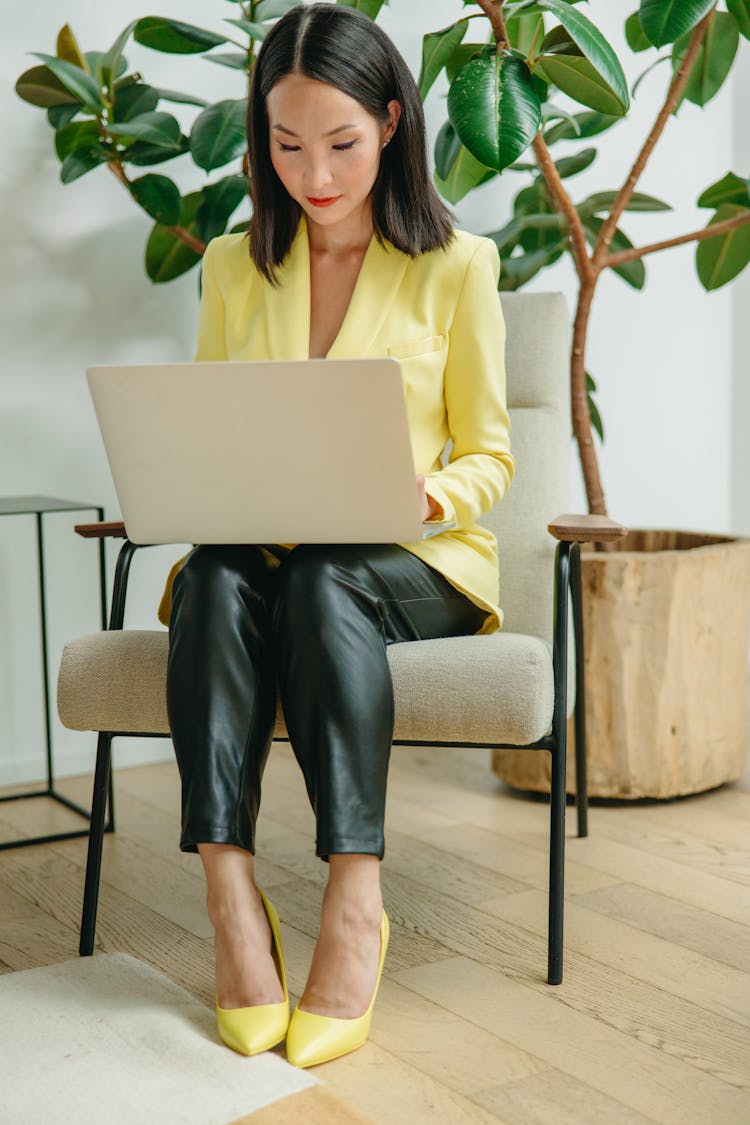 A Woman In A Yellow Blazer And Shoes Using Her Laptop