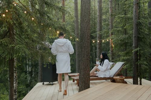 Free A couple enjoying a peaceful retreat in the forest, relaxing in bathrobes amidst nature on a sunny day. Stock Photo