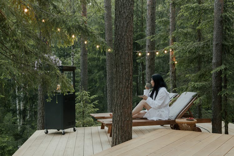 Woman In Bathrobe Sitting On A Lounge Chair While Drinking Beverage