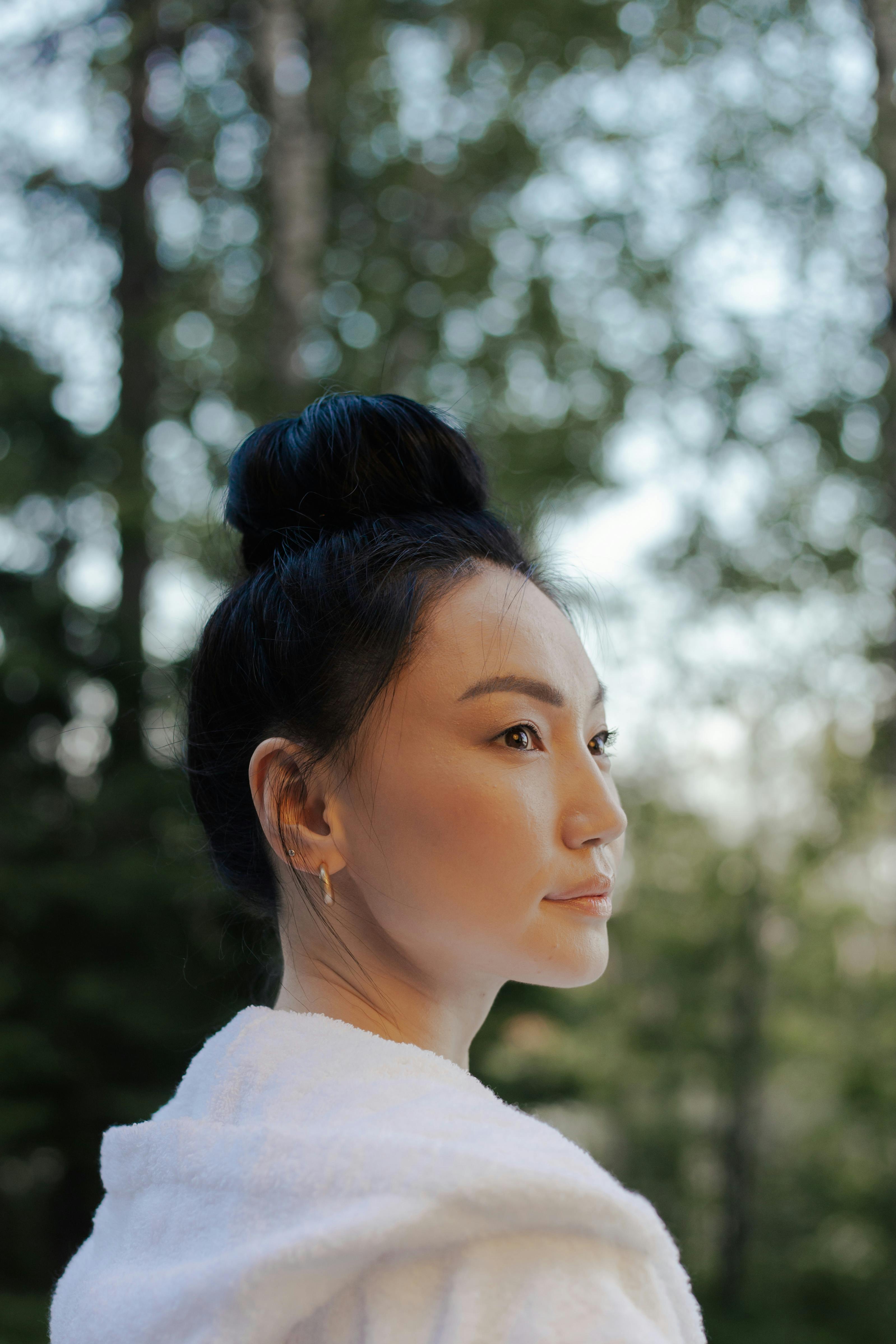 Elegant woman with a hair bun enjoying a peaceful moment outdoors in nature.