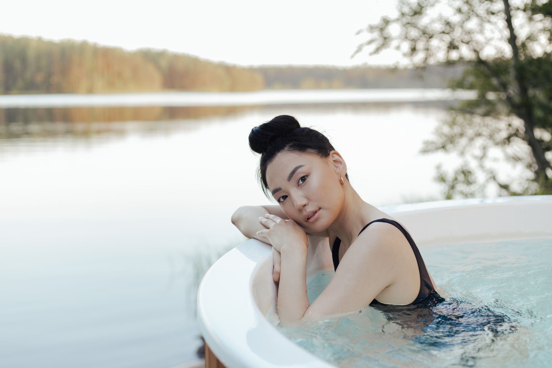 A woman enjoys a relaxing time in an outdoor hot tub by a serene lakeside setting.