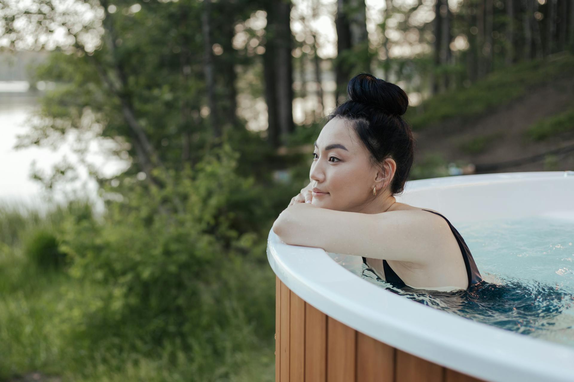 A woman in a swimsuit relaxing in an outdoor hot tub surrounded by nature, embodying leisure and wellness.