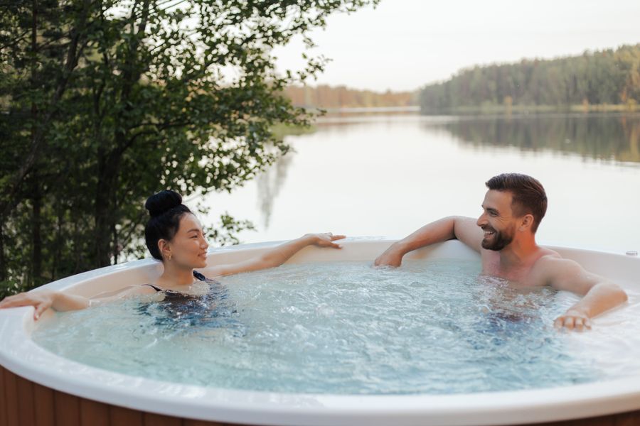 A couple relaxing in an outdoor hot tub beside a calm lake