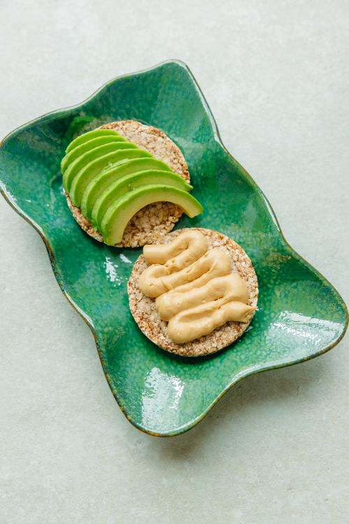 Free Sliced avocado and hummus on rice cakes served on a ceramic plate for a nutritious snack. Stock Photo