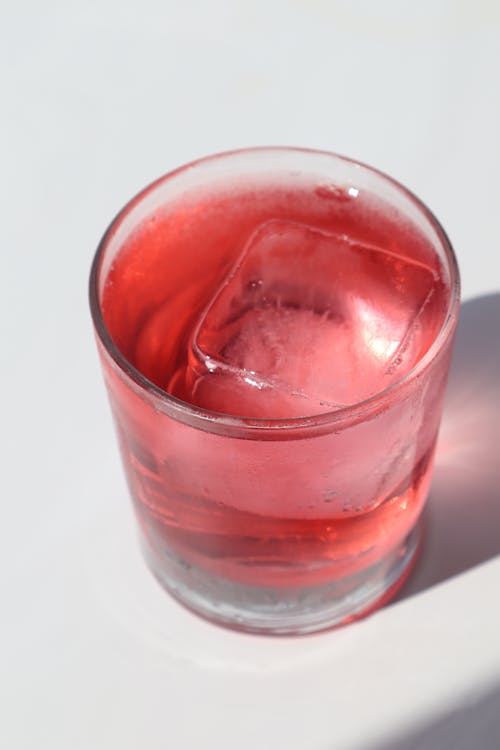 Free From above glass of refreshing red soft drink with ice cube served on white table in sunlight Stock Photo