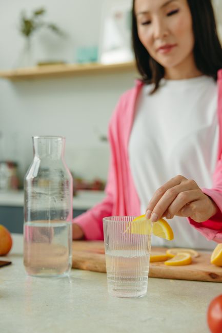 A glass pitcher of pale orange electrolyte water with lemon and orange slices floating inside, next to a filled glass with ice.