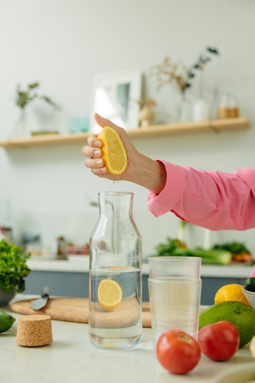 Free A Person Squeezing an Orange in a Glass Pitcher with Water Stock Photo