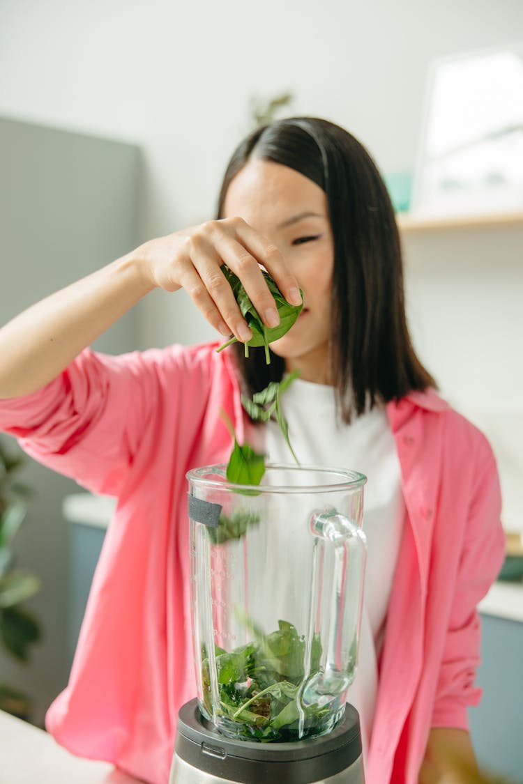 A Woman Dropping Greens In A Blender