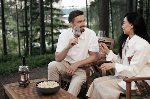 A Couple Sitting on Wooden Chairs Holding Glasses of Wine