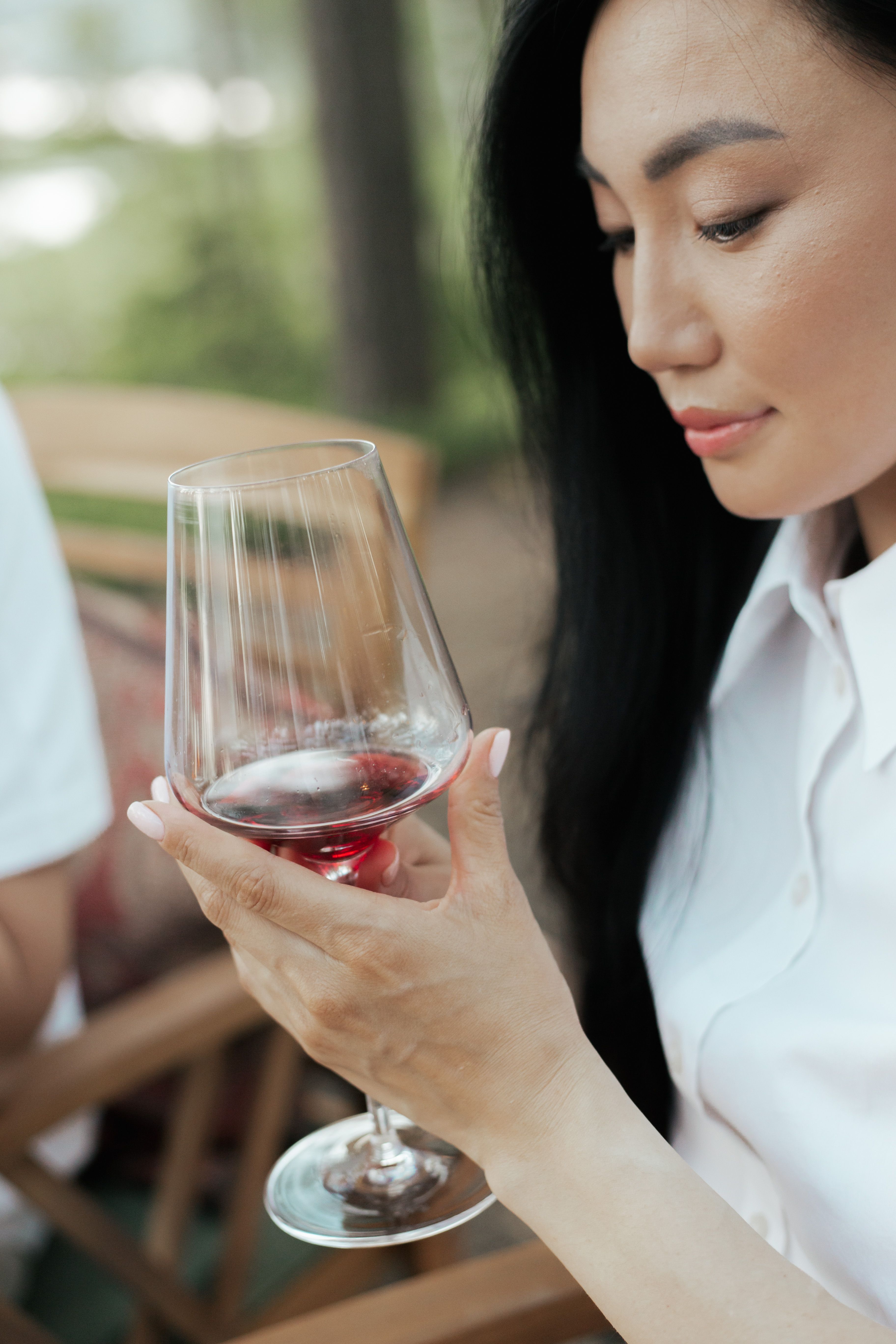 Close-up of an Asian woman savoring red wine in a casual setting.