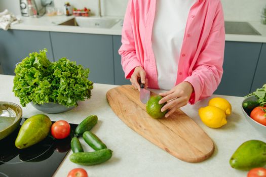 Person in pink shirt chopping vegetables on a wooden board, surrounded by fresh produce.