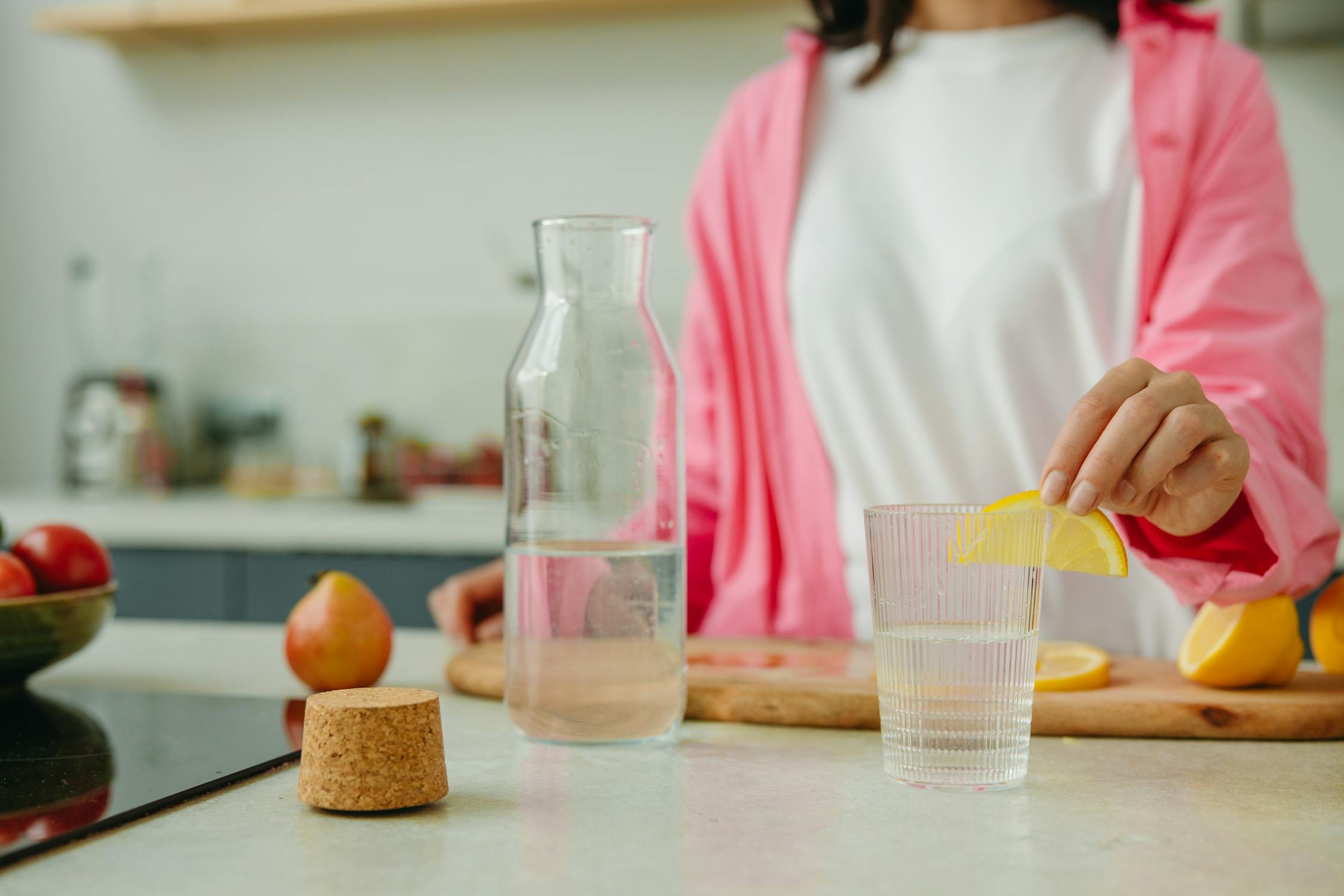 Woman Putting Sliced Lemon on a Glass of Water for hydration, the debate of cold vs. warm water remains
