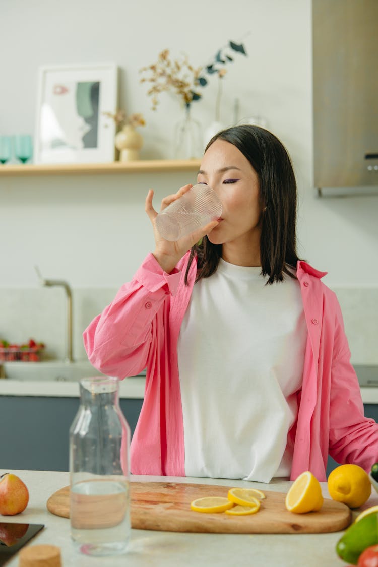 A Woman In A Pink Overshirt Drinking A Water From The Glass