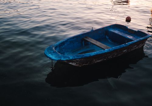 Free An old blue rowboat gently floating on calm waters at sunset, evoking peace and tranquility. Stock Photo