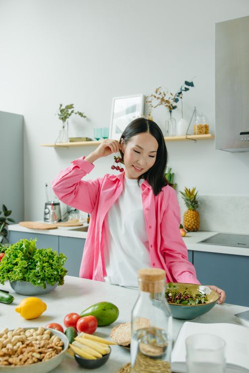 Free Asian woman in kitchen preparing a healthy meal with fresh fruits and vegetables on the countertop. Stock Photo
