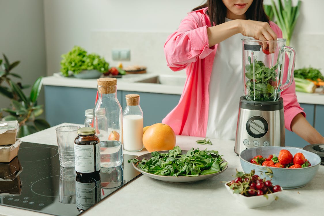 Free A Woman Putting the Green Leaves and Strawberries in the Blender Stock Photo