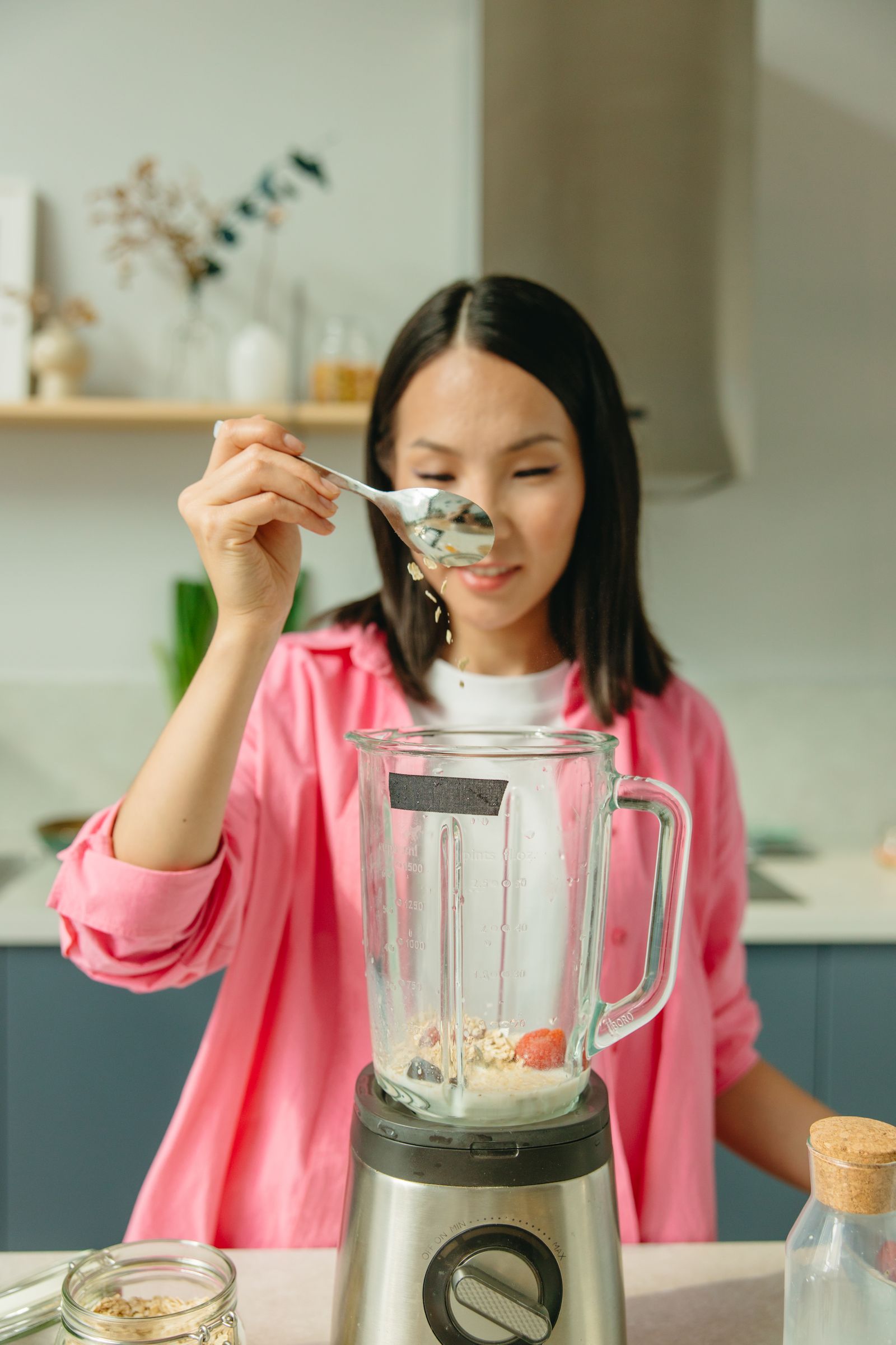 Woman preparing a smoothie with a countertop blender and fresh ingredients in a bright kitchen