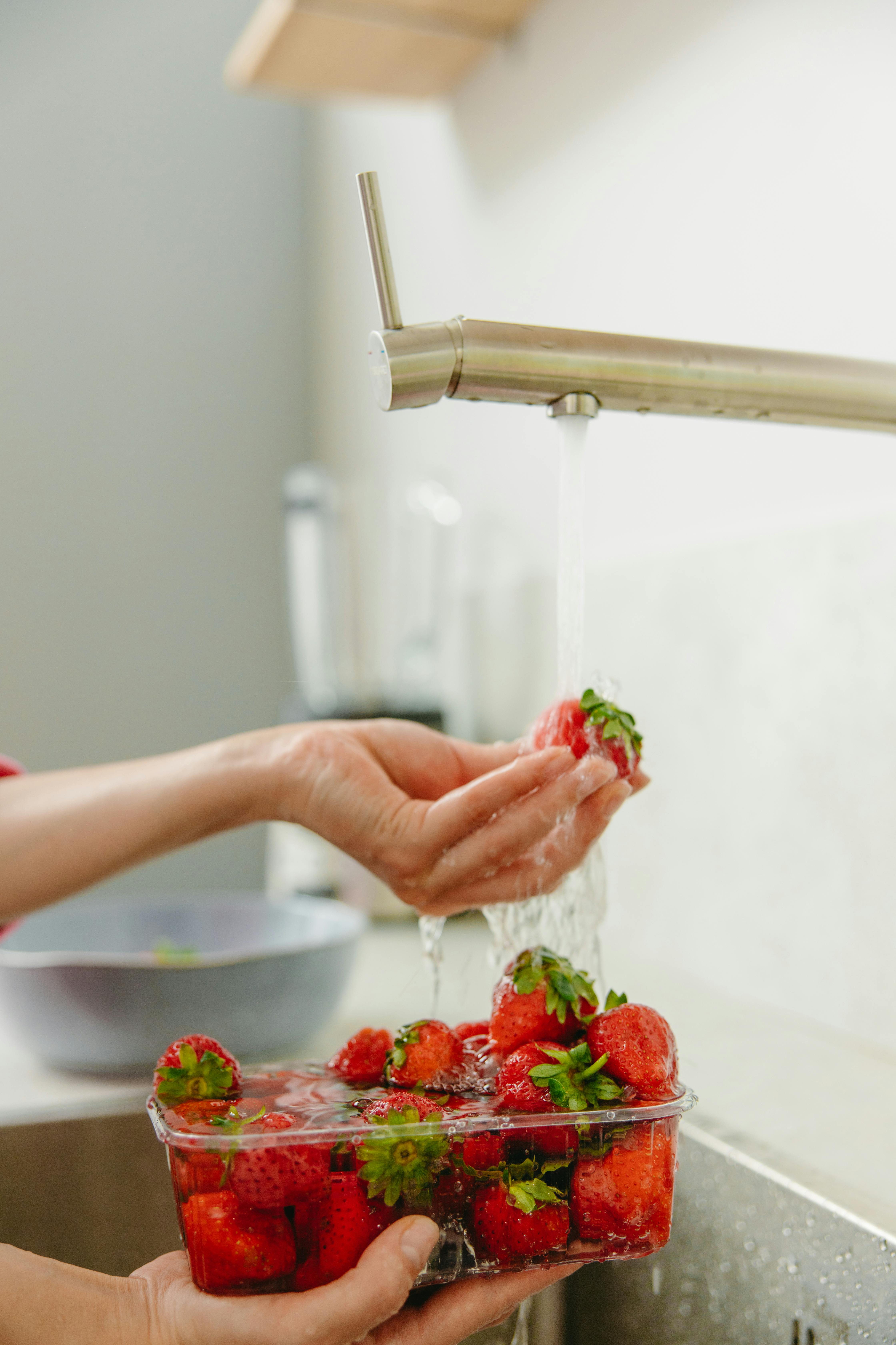 Fresh strawberries being rinsed under a kitchen faucet for cleanliness.