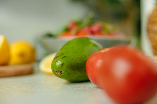 Close-up of fresh avocado and red tomato with blurred lemons in the background, emphasizing healthy food.