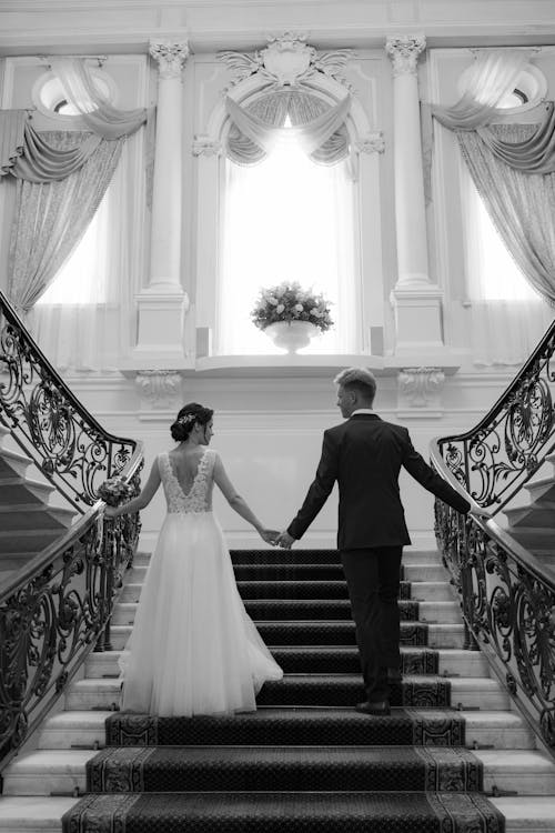 Grayscale Photo of Bride and Groom Walking on Staircase