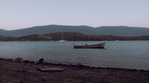 Free A serene view of a boat floating on a calm lake in Muğla, Türkiye, surrounded by mountains at twilight. Stock Photo