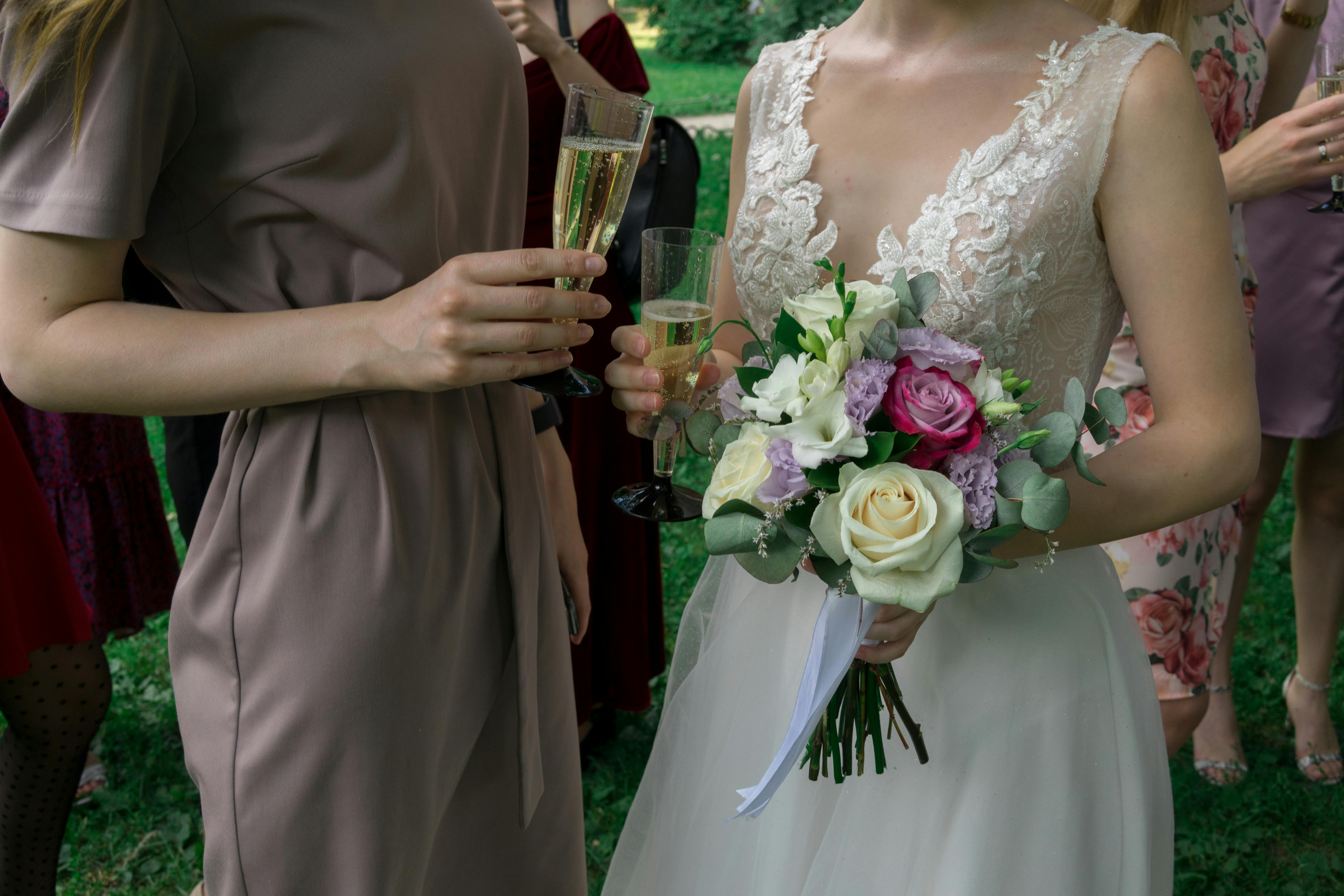 Outdoor wedding celebration with bridal bouquet, champagne, and elegantly dressed women.