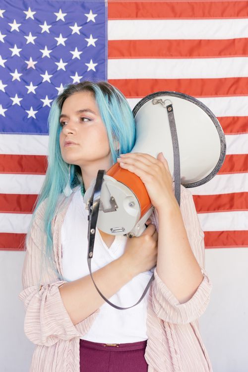 Free Caucasian woman holding megaphone in front of American flag, assertive posture. Stock Photo