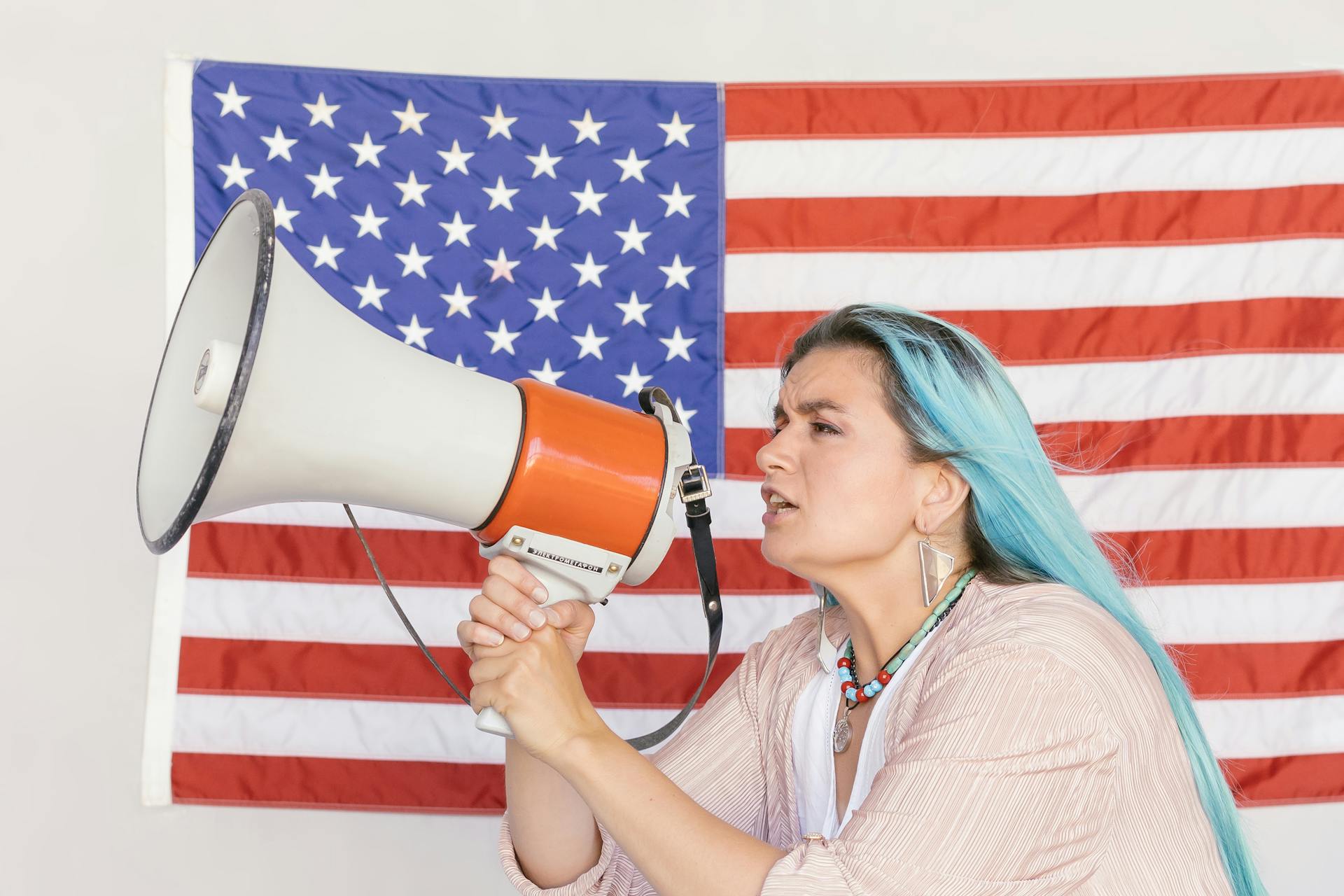 Expressive woman using a megaphone in front of a vibrant American flag, symbolizing freedom.