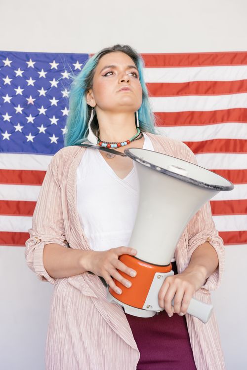 Free Woman stands with megaphone before American flag, symbolizing empowerment. Stock Photo
