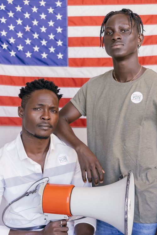 Free Two men pose with a megaphone and vote stickers, in front of an American flag backdrop. Stock Photo