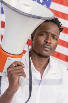 A man holding a megaphone stands in front of an American flag, promoting voting.