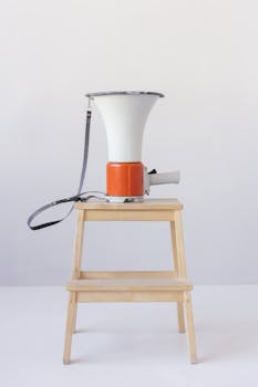 A red and white megaphone placed on a wooden stool against a minimalist background.