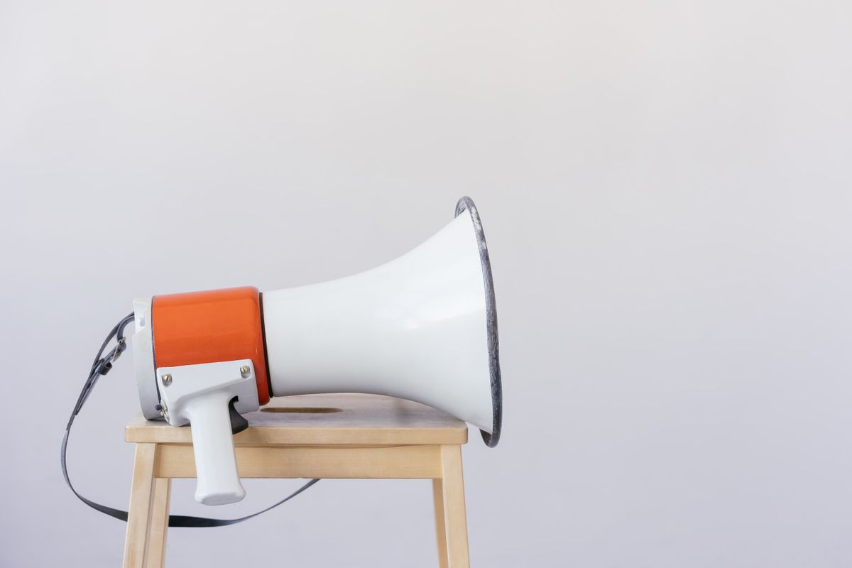 White and orange megaphone resting on a light wooden stool against a plain wall