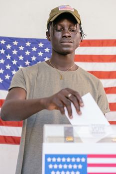 Photo by Mikhail Nilov Young man casting his vote at a polling station with American flag backdrop.