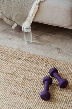 Home workout setup featuring dumbbells, water bottle, and woven mat on wooden floor.