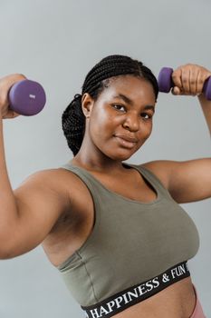 Young woman with braided hair lifting dumbbells, showcasing a fitness lifestyle indoors.