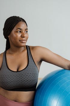 Active African American woman in sportswear with exercise ball indoors.