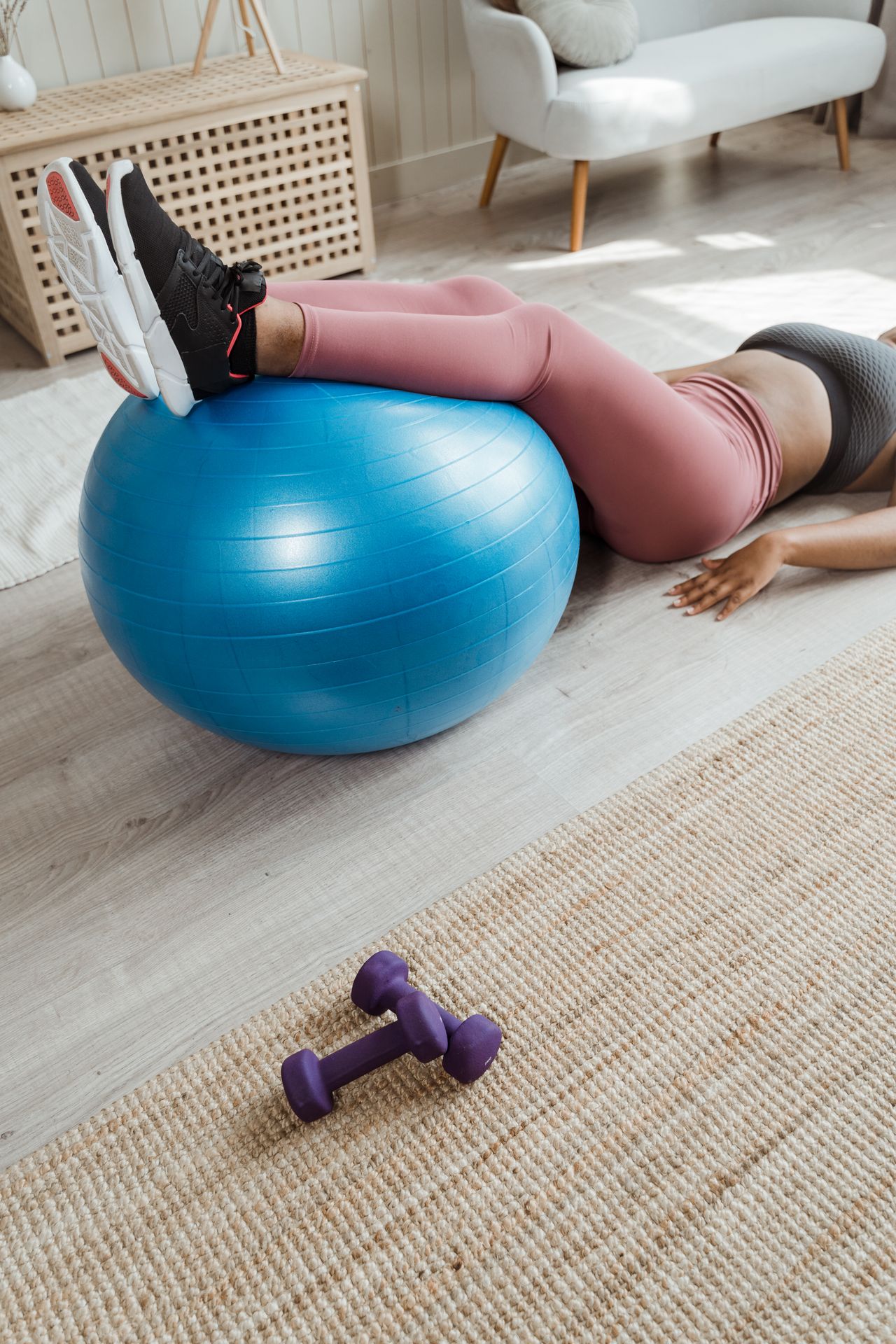 A woman working out at home with a blue stability ball and purple dumbbells for fitness