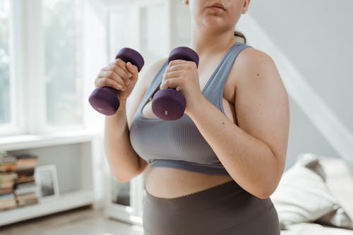 Женщина в сером спортивном бюстгальтере с фиолетовыми гантелями
