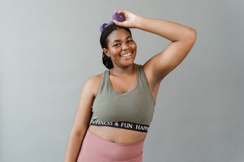 Free A woman in activewear smiling and holding a dumbbell, symbolizing fitness and positivity. Stock Photo