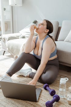A young woman enjoys a snack during a workout at home, reflecting a balanced lifestyle.