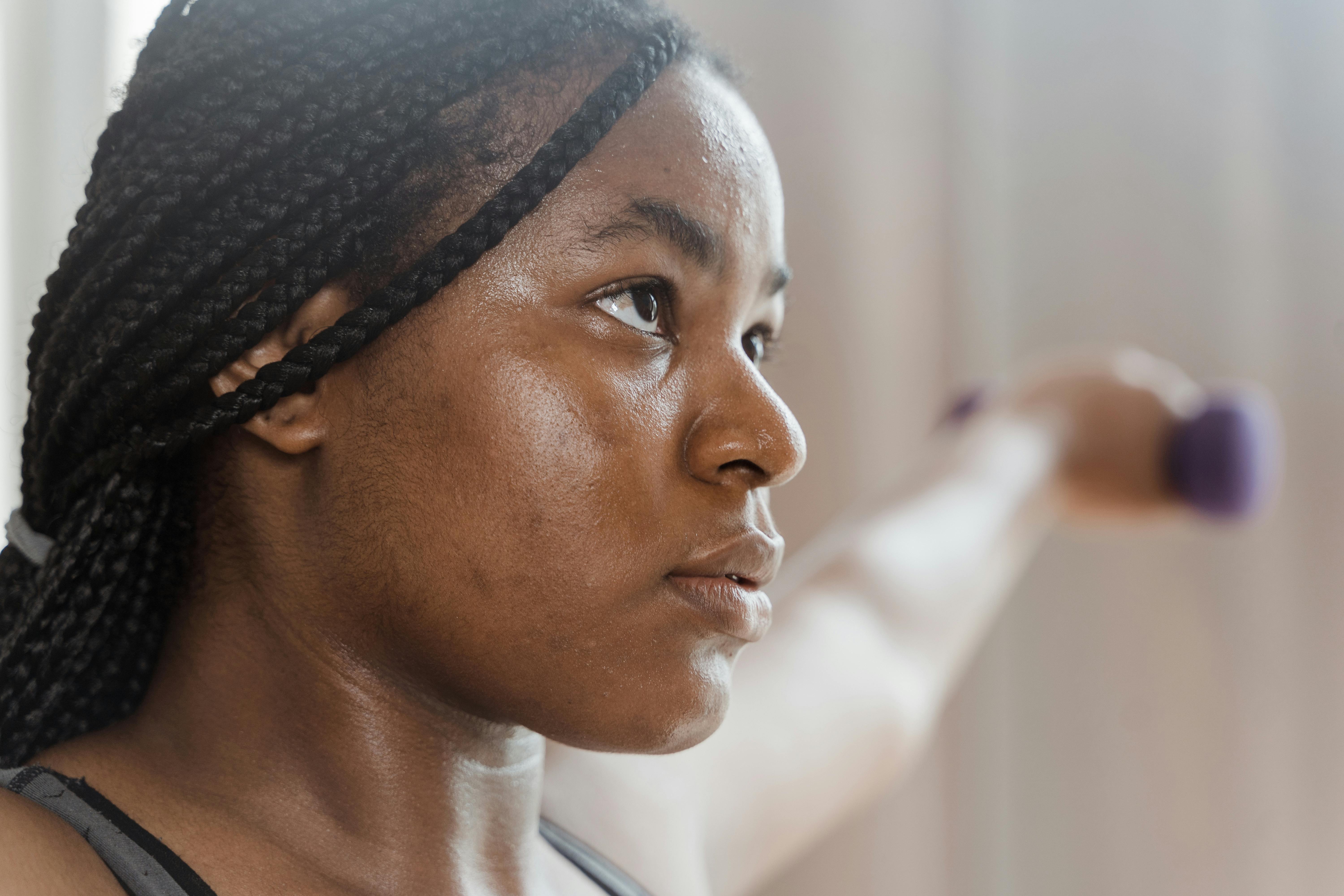 Close-up of a determined black woman lifting a dumbbell indoors.