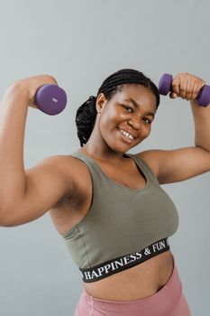 Smiling plus size woman in activewear exercising with dumbbells, promoting body positivity.