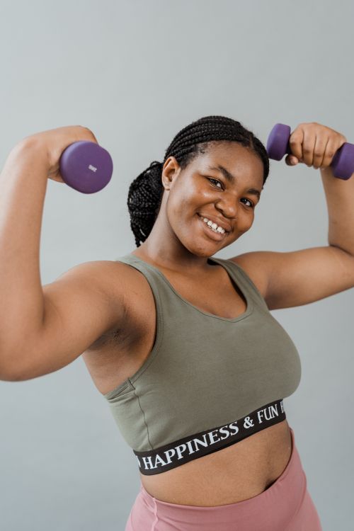 Free Smiling plus size woman in activewear exercising with dumbbells, promoting body positivity. Stock Photo