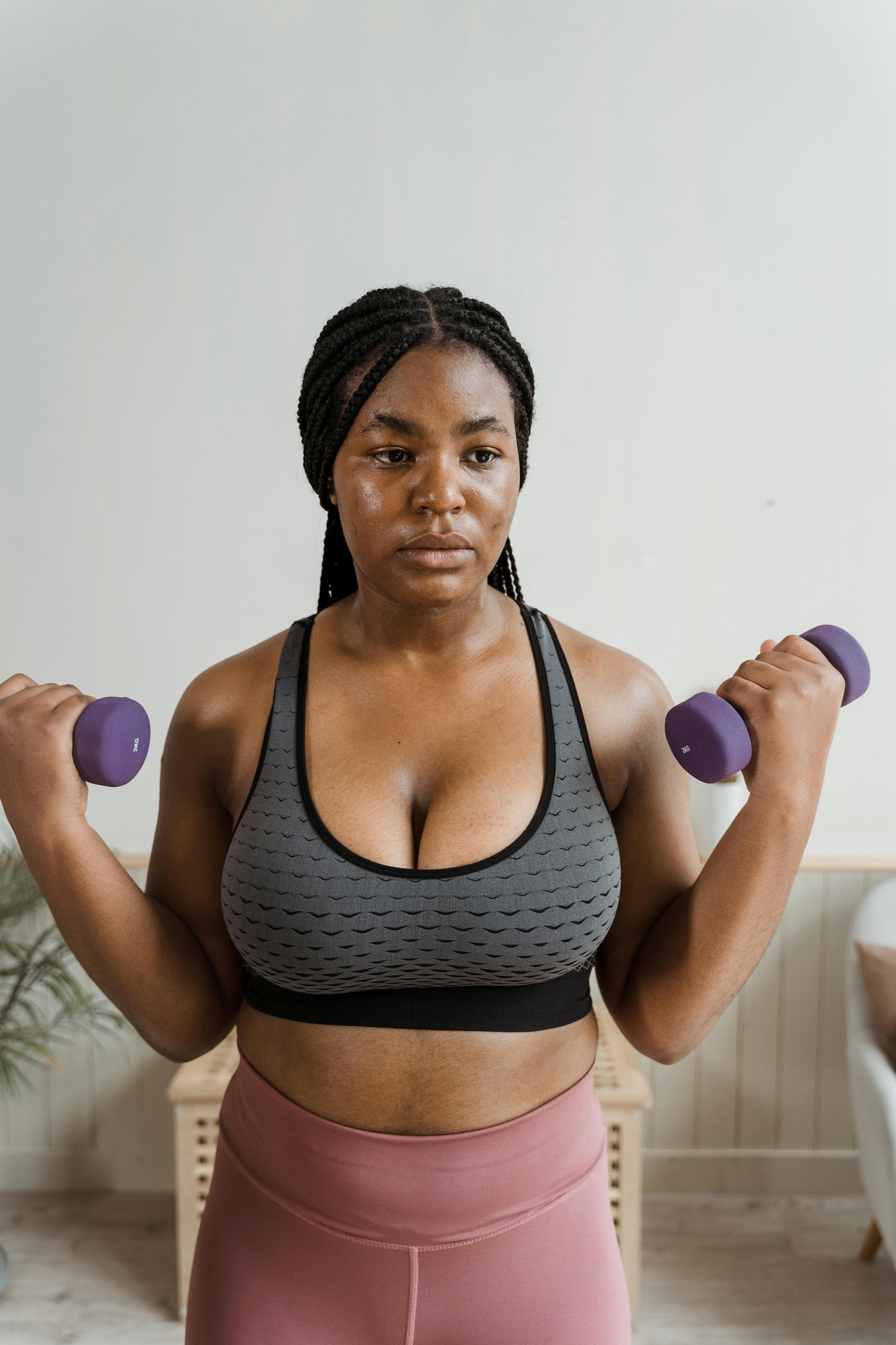 Confident woman in activewear lifting dumbbells indoors, focusing on fitness and strength training.