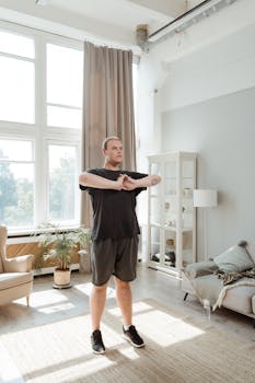 A young man in activewear stretches in a sunlit living room, promoting fitness and wellness.