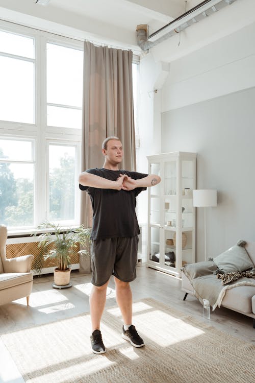 Free Man in Black T-Shirts and Shorts Standing in the Middle of the Room and Warming Up Stock Photo
