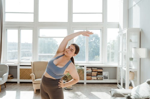 Free Woman in Blue Sports Bra and Gray Leggings Doing Exercises in the Room with Big Window Stock Photo