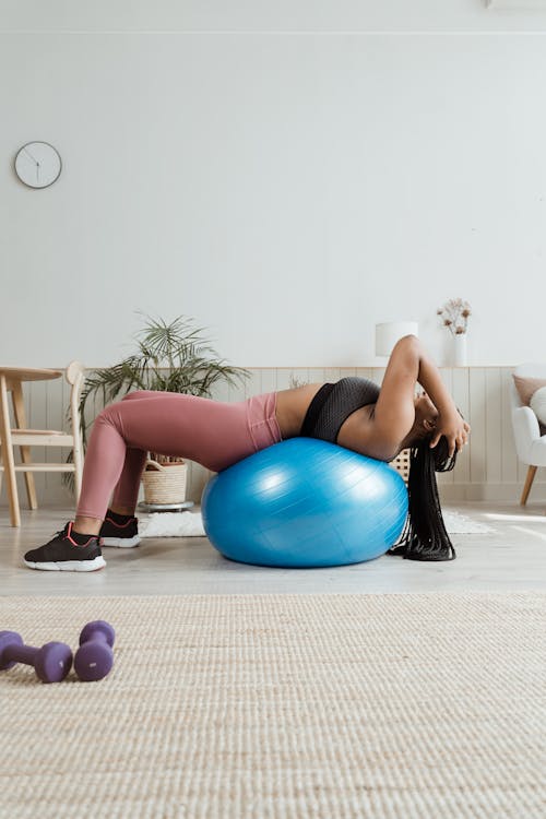 Free Woman in Black Top and Pink Leggings Lying on Blue Fit Ball Stock Photo