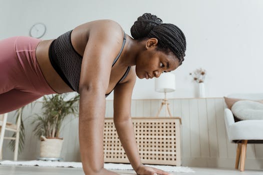 Woman with braided hair doing push-ups indoors, focusing on fitness and strength.